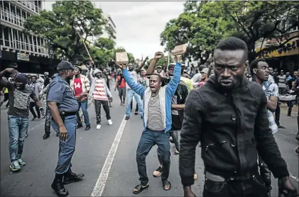  ?? PHOTO : MARCO LONGARI ?? A police officer tries to control a group of Nigerians as they confronted a group of South Africans during a standoff in the centre of Pretoria on Friday. Police fired rubber bullets and stun grenades to break up clashes between the two groups.