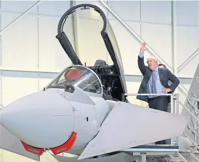  ?? Pictures: PA. ?? Top: Boris Johnson picks up a Tunnocks Teacake during a visit to families in the community centre at RAF Lossiemout­h in Moray; above: The prime minister gets a close-up view of an RAF Typhoon FGR4 at the air base.