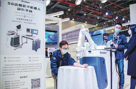  ?? WU ZHIZUN / XINHUA ?? A visitor (left) tries out a 5G ultrasonic robotic system for remote medical consulting at the China 5G+ Industrial Internet Conference in Wuhan, Hubei province, in November.