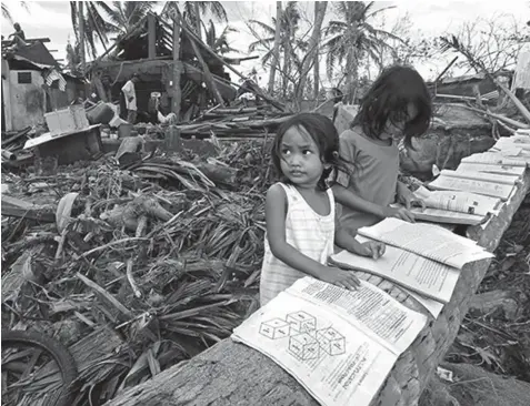  ?? PHILSTAR FILE PHOTO ?? Children read rain-soaked school books being dried on a fallen coconut tree in Barcelona town, Sorsogon. In the background is one of the houses damaged by the typhoon.