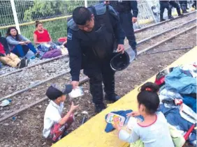  ?? AP PHOTO/MOISES CASTILLO ?? A Guatemalan police officer gives a migrant child some food as the migrants bound for the U.S.-Mexico border wait on a bridge that stretches over the Suchiate River, connecting Guatemala and Mexico, in Tecun Uman, Guatemala, early Saturday. The migrants moved about 30 feet back from the gate that separates them from Mexican police to establish a buffer zone. About 1,000 migrants remained on the bridge between Guatemala and Mexico.