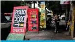  ?? ?? A woman walks between signs with food prices on a street in Buenos Aires. — AFP