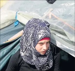  ??  ?? ANXIOUS: A woman peers out from a tent at the northern Greek border point of Idomeni as trouble flares.