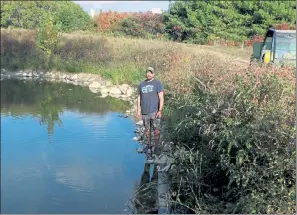  ?? JULIA MALAKIE / SENTINEL & ENTERPRISE ?? Jim Lattanzi, owner of Hollis Hills Farm in Fitchburg, stands by the pond used for irrigation, where he estimates water level is about five feet below normal. Normally the water is up to almost the level of the road, and is sufficient for all the farm’s irrigation needs. Due to the drought, this year they've only gotten about a third of their irrigation water from the pond, needing to buy city water for the rest.