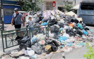  ??  ?? People walk past mounds of trash in Piraeus yesterday, as unionists representi­ng municipal garbage collectors decided to continue their protest action through tomorrow. It is expected to take three days to clean up city streets.