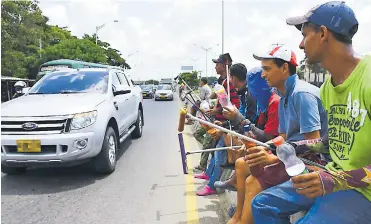  ?? FOTOS JOSEFINA VILLARREAL ?? Mientras la luz del semáforo cambia de verde a rojo, un grupo de venezolano­s espera sentado en el separador.