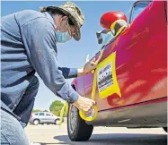  ??  ?? Kevin Tolley tapes a sign to a participan­t's car during the Poor People's Campaign before driving around Congressma­n Jim Inhofe's office in Oklahoma City, Okla. on Monday. The caravan demonstrat­ions are taking place in other cities to protest the plans of Senate Majority Leader Mitch McConnell, to hold hearings for the open U.S. Supreme Court justice seat and what caraven leaders said are his efforts to block pandemic relief bills.