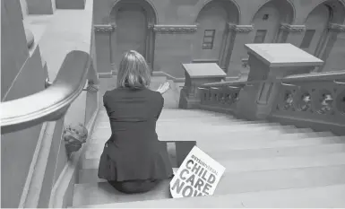  ?? CINDY SCHULTZ/THE NEW YORK TIMES ?? A woman sits at the state Capitol in Albany, New York, alongside a sign calling for universal child care.