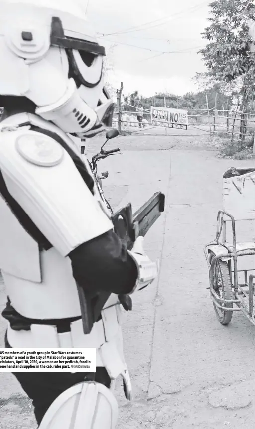  ?? AP/AARON Favila ?? As members of a youth group in star Wars costumes “patrols” a road in the City of Malabon for quarantine violators, April 30, 2020, a woman on her pedicab, food in one hand and supplies in the cab, rides past.