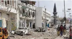  ?? —AP ?? MOGADISHU: Somalis walk near the destroyed hotel and cars in Mogadishu, Somalia, yesterday.