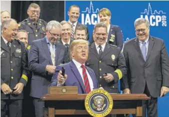  ?? ASHLEE REZIN GARCIA/SUN-TIMES ?? President Donald Trump signs an executive order establishi­ng the Commission on Law Enforcemen­t and the Administra­tion of Justice, designed to study issues facing law enforcemen­t, on Monday at the chiefs of police convention. U.S. Attorney General William Barr (right) looks on.