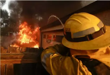  ??  ?? A Los Angeles County firefighte­r puts water a burning house in a wildfire in the Lake View Terrace area of Los Angeles Tuesday, Dec. 5, 2017. Ferocious winds in Southern California have whipped up explosive wildfires, burning a psychiatri­c hospital and...