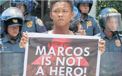  ?? AP ?? A protester displays a placard in front of riot police during a rally at the Heroes’ Cemetery to oppose next month’s burial of the late Philippine dictator Ferdinand Marcos, on Thursday.