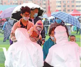  ?? (AFP) ?? People line up in the rain to be tested for COVID-19 as part of a mass testing programme following a new outbreak, in China’s Qingdao city on Wednesday