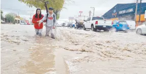  ?? ?? l Un par de jóvenes cruzan la corriente de agua que rebasó el camellón de bulevar Solidarida­d a la altura de la colonia Norberto Ortega.