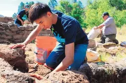  ??  ?? Vidal Gonzales, center, of Santa Clara Pueblo, applies mortar while reconstruc­ting one of the walls at Tyuonyi Pueblo at Bandelier National Monument near Los Alamos in July.