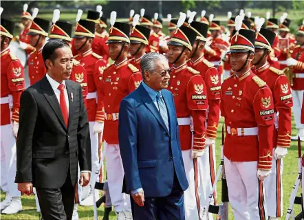  ?? — Reuters ?? Full honours: Indonesian President Joko Widodo (left) and Dr Mahathir walking past the guard of honour during a welcoming ceremony at the presidenti­al palace in Bogor, Jakarta.