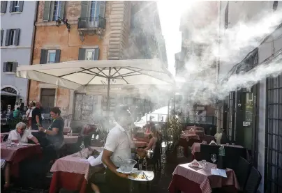  ?? The Associated Press ?? ■ In this July 31, 2020, file photo, a fan sprays water mist as customers sit outside a cafe in downtown Rome during a heat wave with temperatur­es over 34 Celsius (104 Fahrenheit).