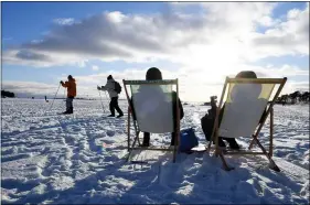  ?? JUSSI NUKARI — LEHTIKUVA VIA AP ?? People sit in the sunshine as others ski by, during a sunny winter day on waterfront ice of Helsinki, Finland on Valentine’s Day Feb. 14. In a year of untimely deaths from the coronaviru­s, economic decline and social loneliness, people have been resilient.