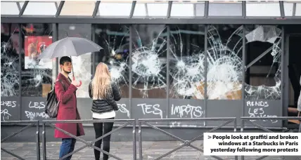  ??  ?? &gt; People look at graffiti and broken windows at a Starbucks in Paris yesterday following more protests