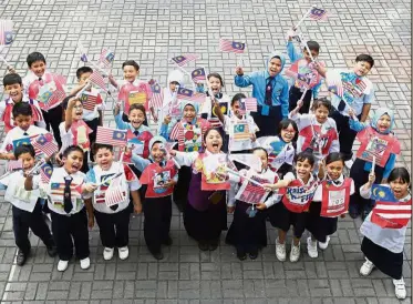  ??  ?? We love Malaysia: Class 3 Marikh pupils raising the Jalur Gemilang they assembled and wearing their decorated T-shirt cutouts at the school compound in Petaling Jaya.