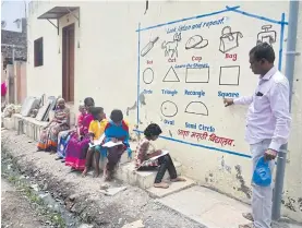  ??  ?? Teacher Kalidas Chavdekar points to excerpts from textbooks on various subjects painted on the wall of a house to teach students who lack internet access for online classes in Nilamnagar.