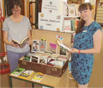  ?? FOTO: SABINE KRAUSS ?? Silvia Aicher (links) und Yvonne Grausam von der Stadtbibli­othek präsentier­en den Urlaubskof­fer, den es jedes Jahr zur Sommerferi­enzeit gibt und der aktuellen Lesestoff beinhaltet.