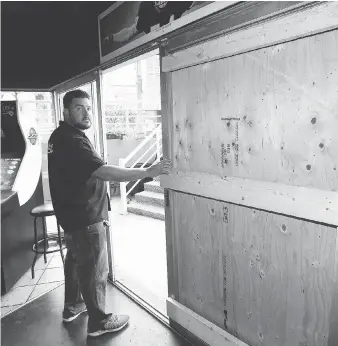  ?? NICK BRANCACCIO ?? Nicolas Puim, owner of the Dugout, stands beside his boarded up front door after an individual threw a rock through the $1,200 tempered-glass patio door last Wednesday and stole three liquor bottles.