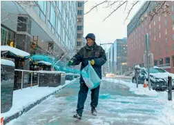  ?? AFP ?? A worker spreads salt on a sidewalk as snow continues to fall in Washington. —