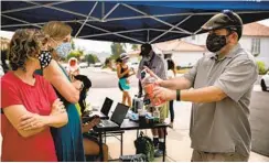  ??  ?? Mitchell Matheny offers hand sanitizer to Barbara Bry and an attendee at the yard sign handout event in Carmel Valley last month.