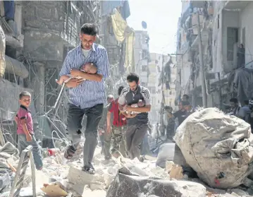  ?? AFP ?? Syrian men carrying babies make their way through the rubble of destroyed buildings following a reported air strike on the rebel-held Salihin neighbourh­ood of Aleppo on Sept 11, 2016.