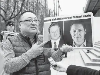  ?? JASON REDMOND • AFP VIA GETTY IMAGES ?? Louis Huang, of Vancouver Freedom and Democracy for China, holds photos of Canadians Michael Spavor and Michael Kovrig, who are being detained by China. The two men have been charged and may face life imprisonme­nt for espionage.