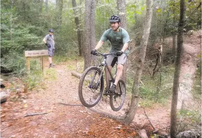  ?? David Hopper / For the Houston Chronicle ?? Cypress resident Mitch Callihan jumps an obstacle, after cycling through a creek on bike trails at the 100 Acre Wood Preserve, 10602 Normont. The preserve has two miles of trails through rolling, forested terrain. Watching is Bill Collier, incoming...