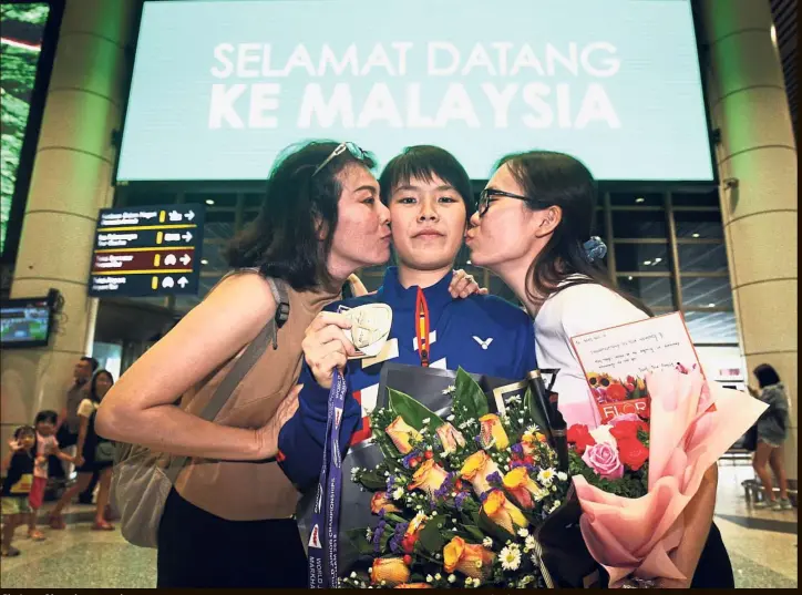  ?? — FAIHAN GHANI / The Star ?? She’s an Olympic contender: World Junior girls’ singles champion Goh Jin Wei is kissed by her mother Loh Bee Sim (left) and sister Goh Jin Mei at the Kuala Lumpur Internatio­nal Airport in Sepang yesterday.