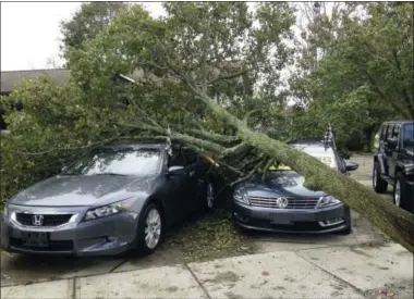  ?? JENNIFER MCDERMOTT — THE ASSOCIATED PRESS ?? A toppled tree covers cars for sale at Demo’s Auto Sales after an overnight storm Monday in Warwick. R.I. Falling trees knocked down power lines across the region, and some utility companies warned customers that power could be out for a few days.