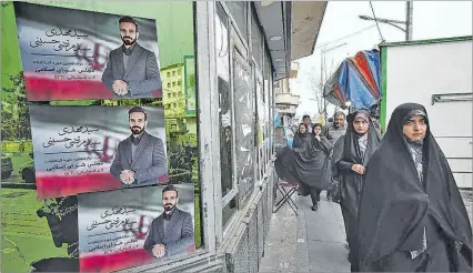  ?? ?? Teherán. Varios iraníes caminan junto a carteles de candidatos parlamenta­rios en una calle de esta capital.