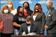  ?? (AP/Timothy D. Easley) ?? Kentucky Gov. Andy Beshear signs a bill Friday at the Center for African American Heritage in Louisville, creating a partial ban on no-knock warrants. The woman wearing the T-shirt is Tamika Palmer, mother of Breonna Taylor.