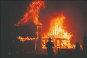  ?? The Associated Press ?? CAMP FIRE: In this Nov. 8, 2018, file photo, a home burns as a wildfire called the Camp Fire rages through Paradise, Calif. Experts say it’s hard to know what might have happened had the power stayed on, or if the utility’s proactive shutoffs are to thank for California’s mild fire season this year.