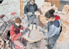  ??  ?? From left, Jonas Rakete, Severin Stavinoha and Serena Bjornson clean bricks of mortar before they are stacked.