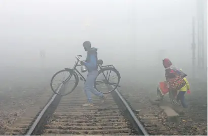  ?? AFP ?? A family crosses a railway track in dense fog conditions in Jalandhar on Tuesday. —