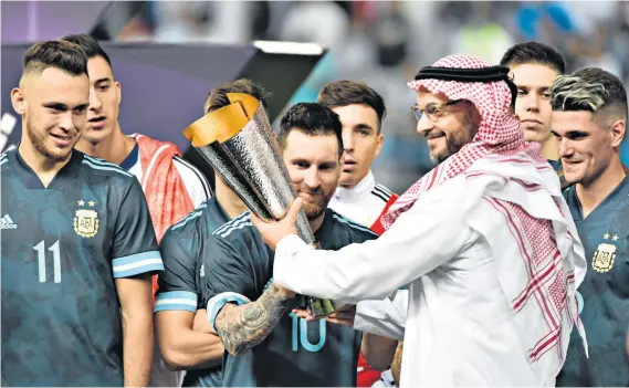  ?? ?? Trophy hunters: Lionel Messi, now the face that stares out from the desert billboards of Saudi Arabia, is handed the cup after a friendly between Argentina and Brazil in Riyadh in 2019