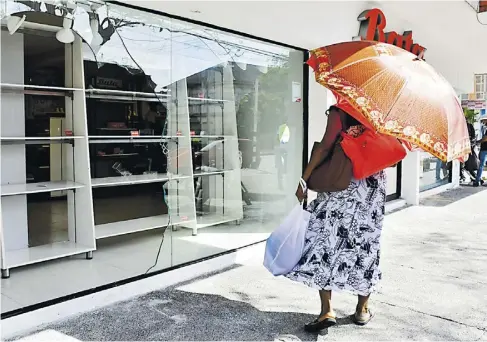  ?? LUIS RODRÍGUEZ Y CORTESÍA ?? Una mujer transita por la calle 72 y observa una tienda que fue vandalizad­a la noche del jueves.