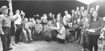  ??  ?? Dennis (squatting, left) blows the candles on the Christmas cake as members of Sarawak Society of the Disabled, Miri branch, friends and relatives cheer.