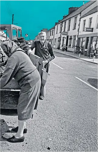  ?? Picture Philip Dunn ?? A woman collects a bag of peat for her kitchen fire from a street delivery man in Ireland in 1990