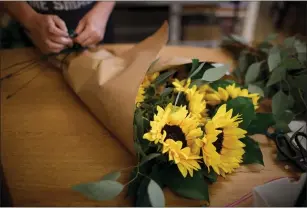  ??  ?? A bouquet of sunflowers is prepared at Fremont Flowers and Gifts, which opened part of its store to walk-in customers on Friday.