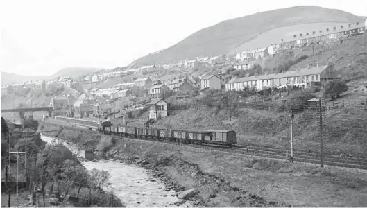  ?? S Rickard/J & J Collection ?? Another of the 0-6-0PTs designed by F W Hawksworth, No 8460 of Treherbert shed, is working turn T13. It has picked up loaded mineral wagons from Lewis Merthyr Colliery at Trehafod and is heading up the valley past the signal box and station at Dinas Rhondda on the middle road, which was a feature of the valley, again on Saturday, 12 May 1956. The final destinatio­n of the train is unknown. The engine had arrived at Treherbert in March 1953 and it would be moved on to Radyr shed in June 1958. Lewis Merthyr is recalled for its Bertie and Trefor pits and would bring coal to the surface until 1958, when merged with Tymawr. Retained for the supply of materials for its sister pit, that role continued through to June 1983 and thus enabled the pithead gear to survive into preservati­on as part of the Rhondda Heritage Park.