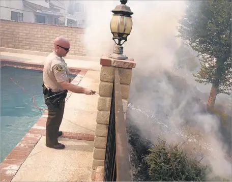  ?? Robert Gauthier Los Angeles Times ?? JASON VIGER, an L.A. County sheriff’s deputy, hoses down a hot spot as a fast-moving brush fire threatens a Newhall home in July.