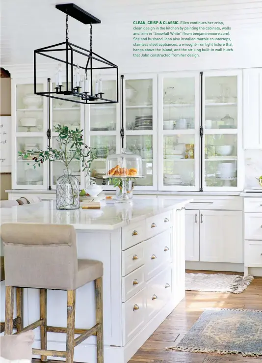  ??  ?? CLEAN, CRISP & CLASSIC. Ellen continues her crisp, clean design in the kitchen by painting the cabinets, walls and trim in “Snowfall White” (from benjaminmo­ore.com). She and husband John also installed marble countertop­s, stainless steel appliances, a wrought-iron light fixture that hangs above the island, and the striking built-in wall hutch that John constructe­d from her design.