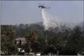  ?? GREGORY BULL — THE ASSOCIATED PRESS FILE ?? A helicopter drops water near a structure as crews fight the Skyline Fire in San Diego County near Jamul.