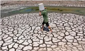  ?? Photograph: Nhac Nguyen/AFP/Getty Images ?? A man shields from the sun as he crosses a dried-up pond in Vietnam in March, which was recorded as the hottest month globally on record.